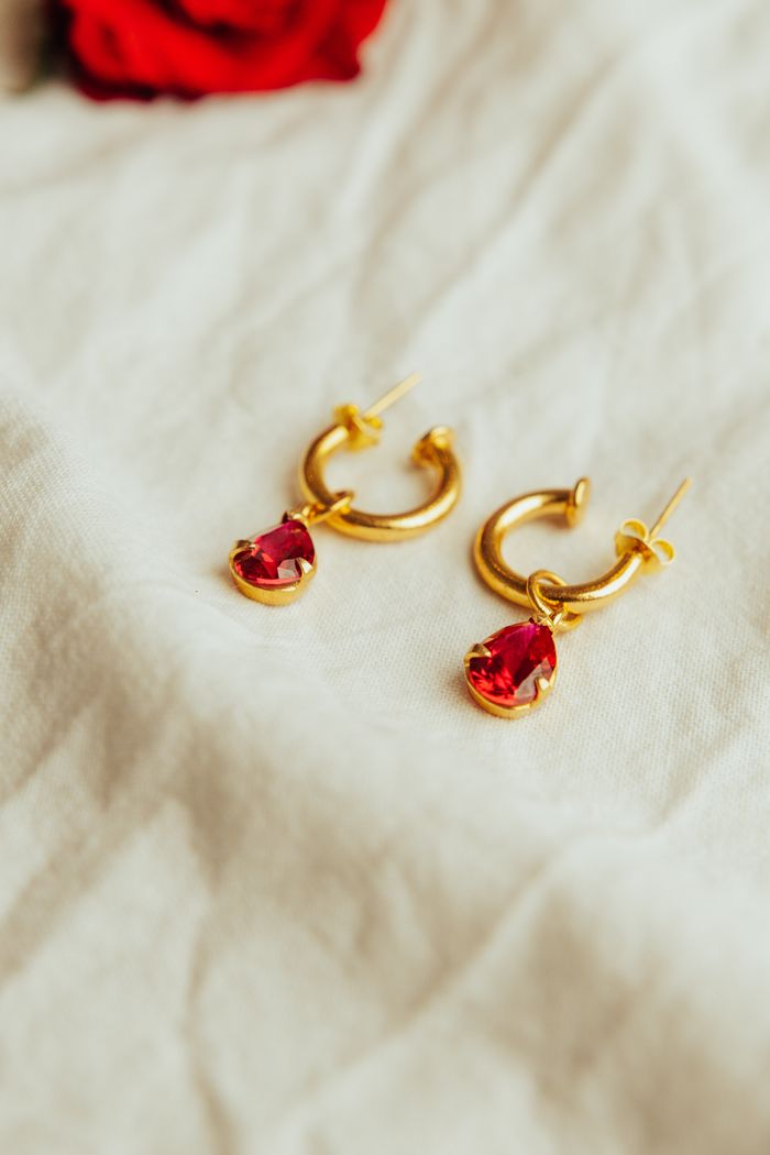 Services Close-up shot of gold earrings with red gemstones on white fabric, exuding luxury and elegance.