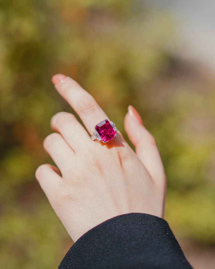 Services Close-up of a hand showcasing a pink gemstone ring, lit by natural daylight.