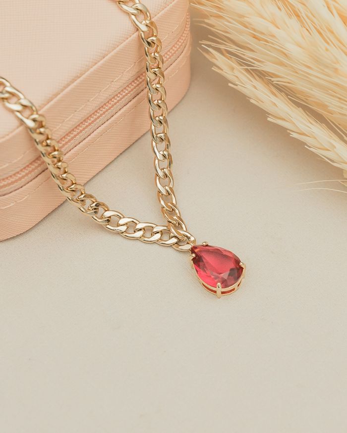 Gold chain necklace with a ruby pendant on a beige jewelry box.